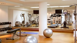 Un gimnasio con diferentes máquinas de ejercicio, una banca, mancuernas y pelotas de gimnasia.