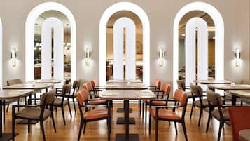 Un ristorante con diversi tavoli e sedie, finestre ad arco e illuminazione a parete.