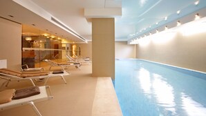 Piscina interior con sillones de descanso y una pared de cristal.