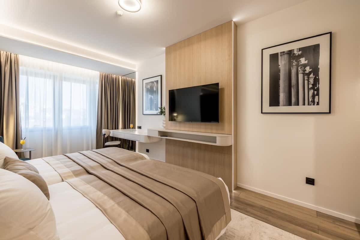 Habitación de hotel moderna con una cama grande, un escritorio con silla, un televisor de pantalla plana en la pared y un cuadro enmarcado sobre el televisor.