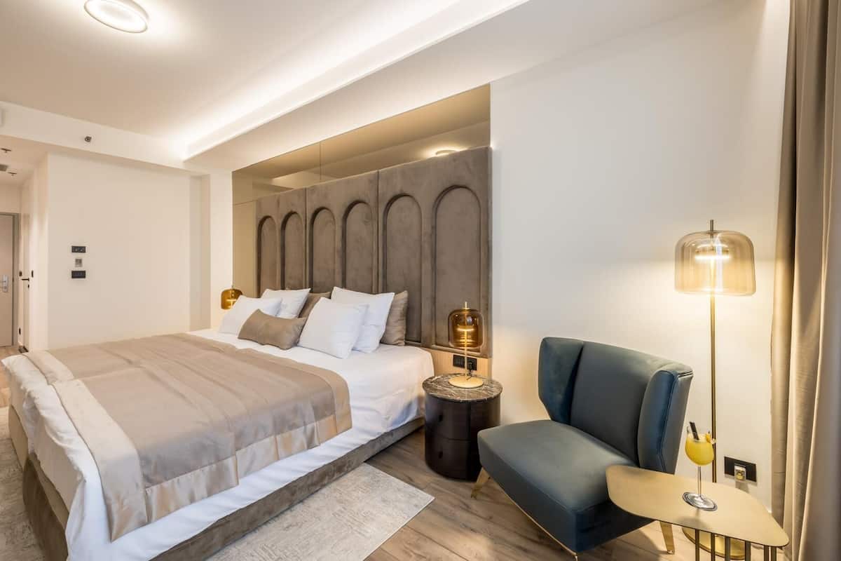 Una habitación de hotel moderna con una cama grande, una zona de estar y una lámpara de pie.