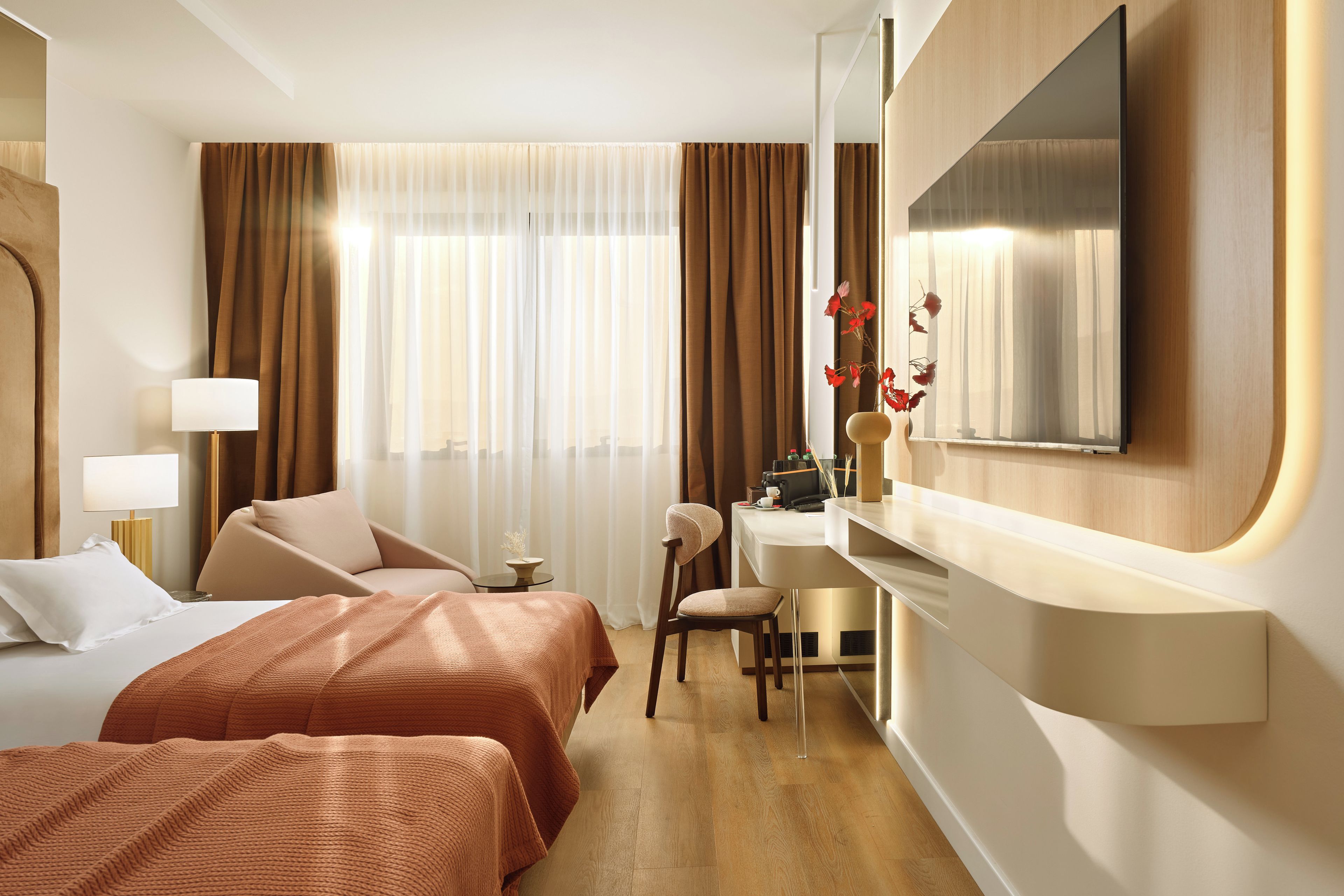 A hotel room with two beds, a desk, a chair, a mirror, and a window with curtains.