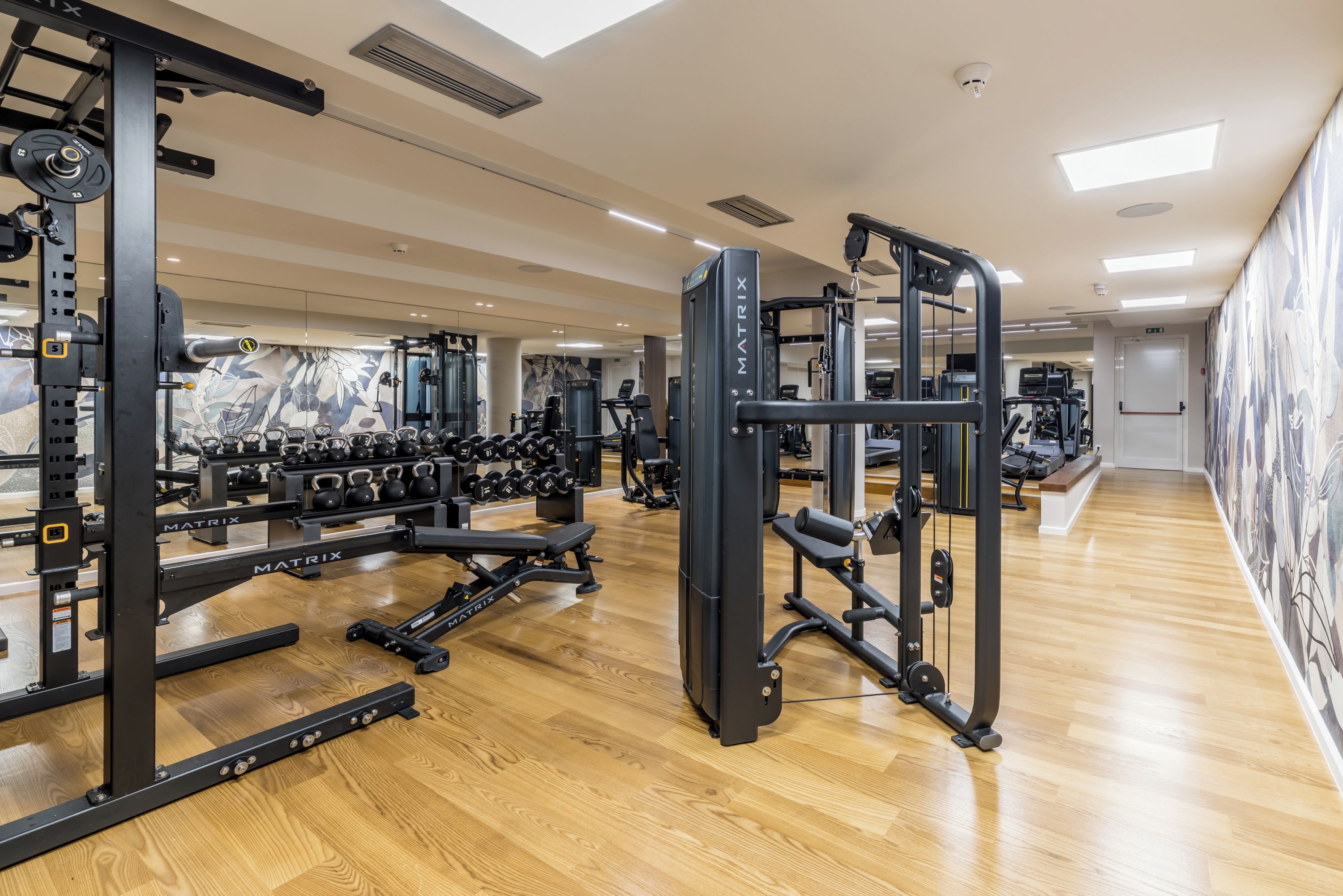 Een sportschool met diverse fitnessapparatuur, houten vloeren en een spiegelwand.