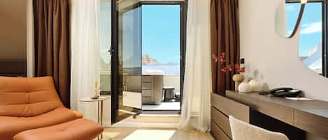 Une chambre d’hôtel moderne, dotée d’un canapé, d’un bureau avec un téléphone et offrant une vue sur la ville par la porte ouverte.