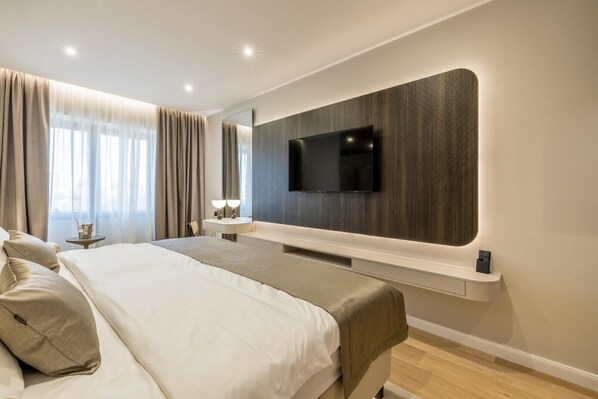 A modern hotel bedroom with a large bed, a mounted TV, and a bedside table with a lamp.