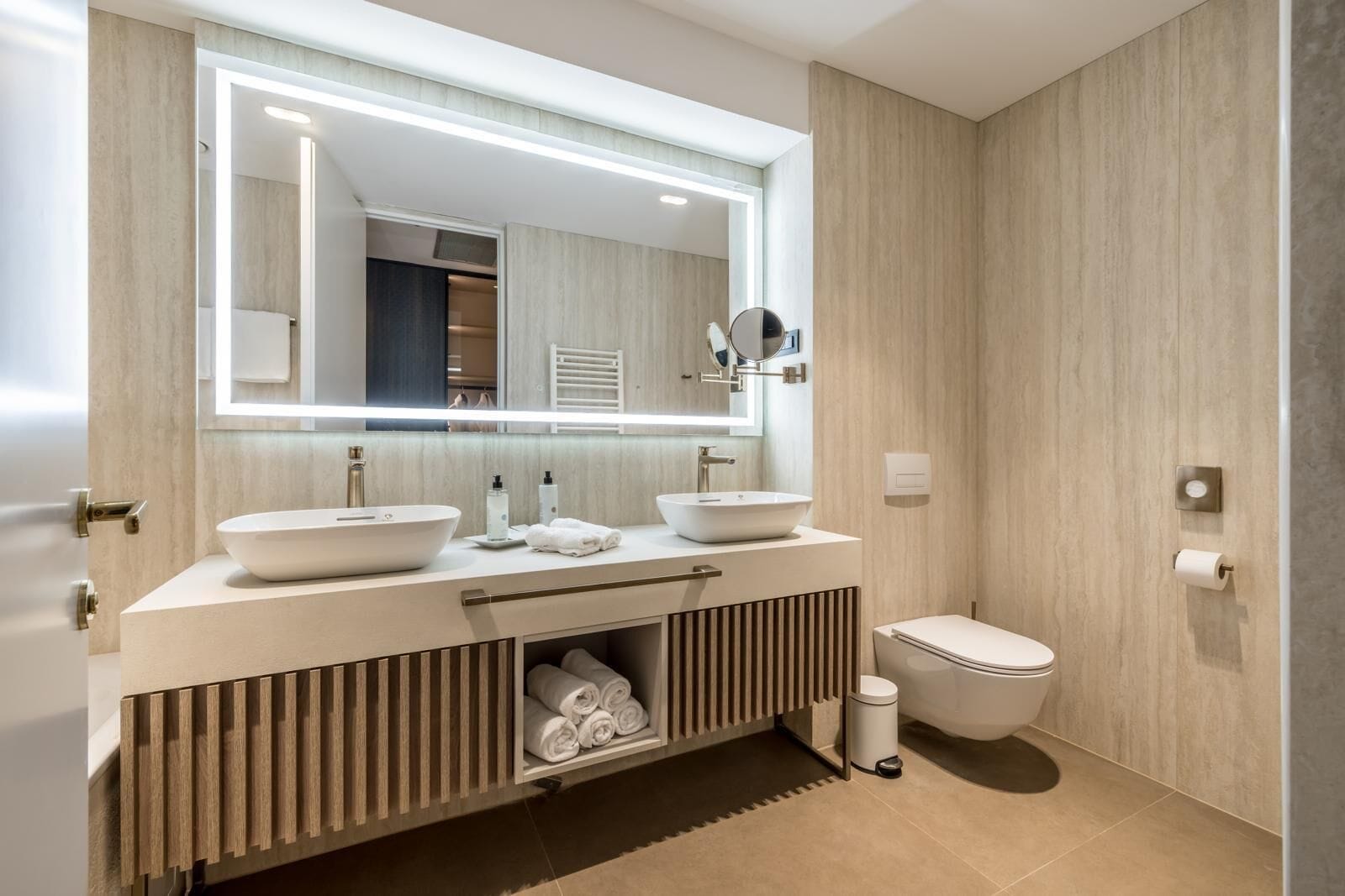 Un baño moderno con dos lavamanos, un inodoro y un mueble de tocador con toallero.