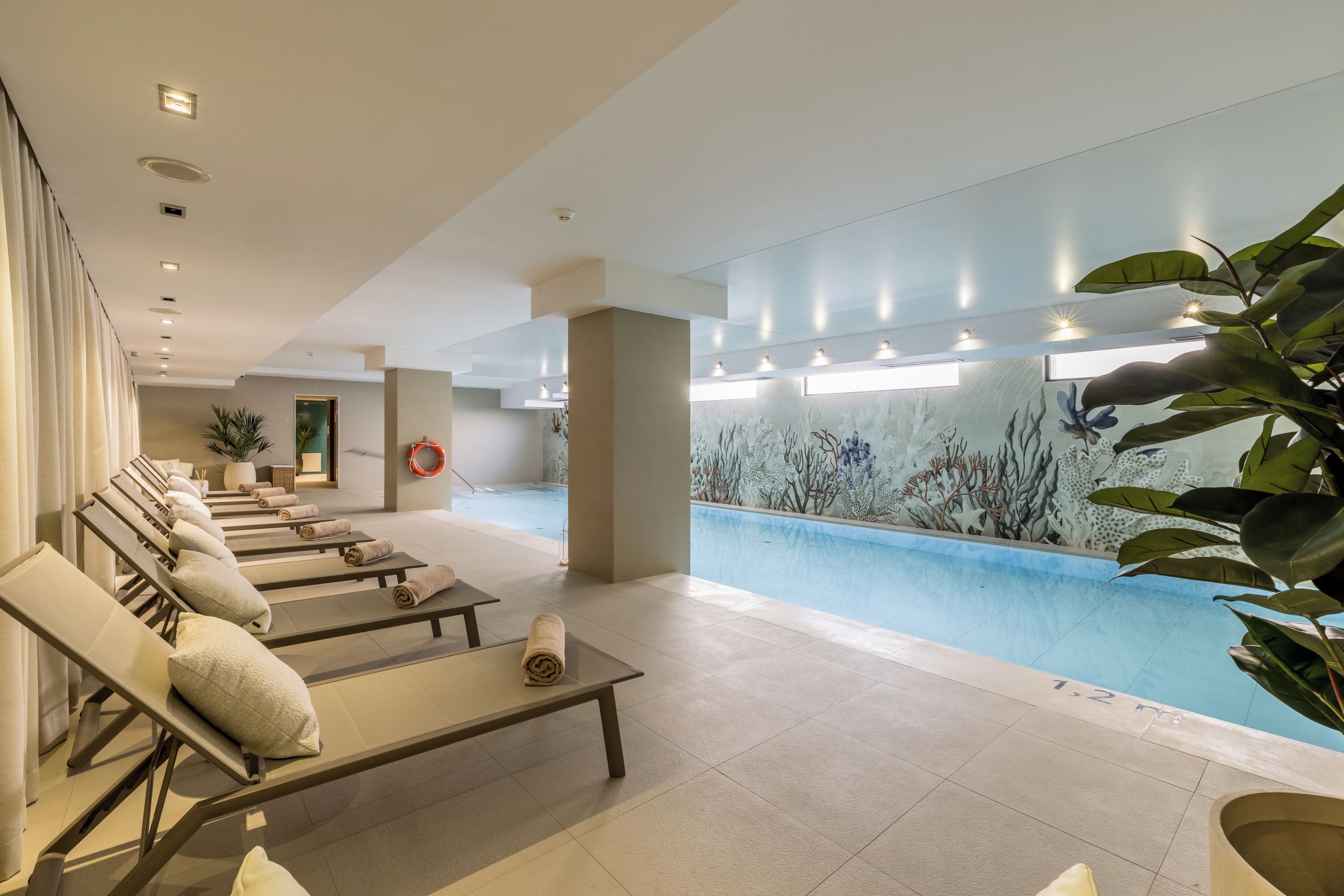 Un hall d’hôtel avec un espace piscine, des chaises longues et une fresque murale.
