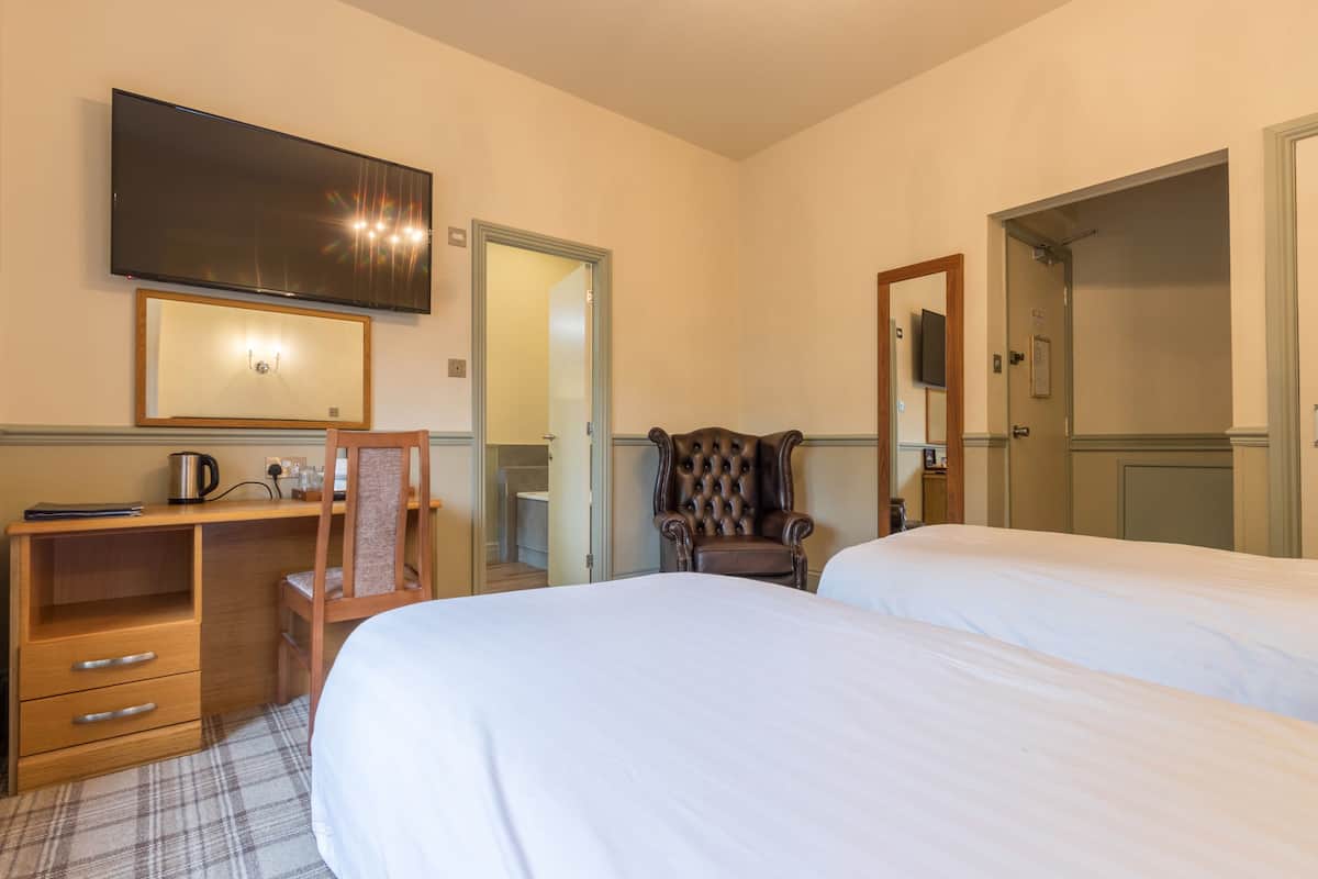 A hotel room with two beds, a desk with a chair, a television, and a mirror.