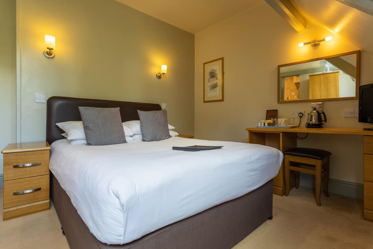 A hotel room with a large bed, bedside tables, a desk with a chair, a mirror, and a television.