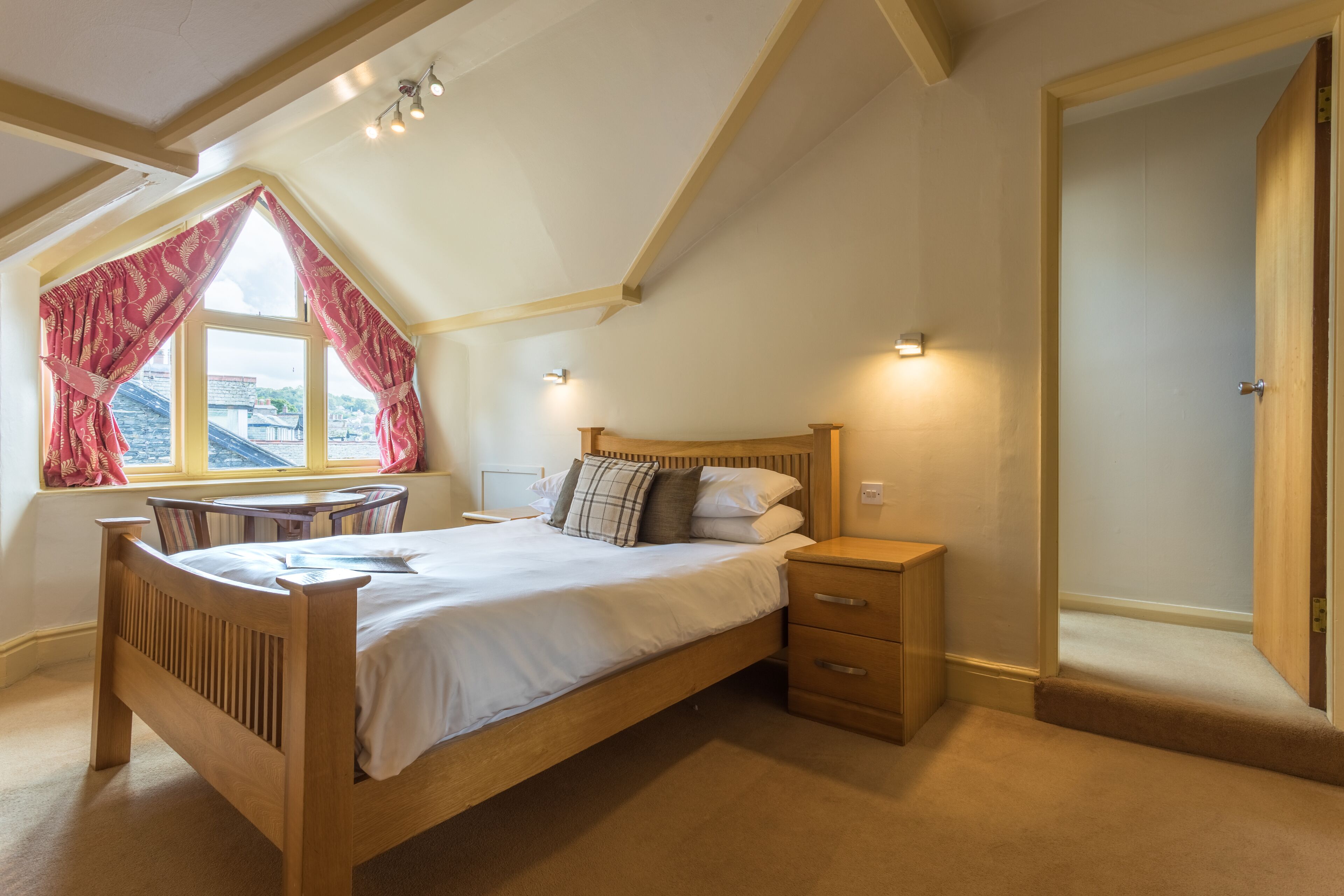 A bedroom with a wooden bed, bedside tables, a window with curtains, and a view of the outside.