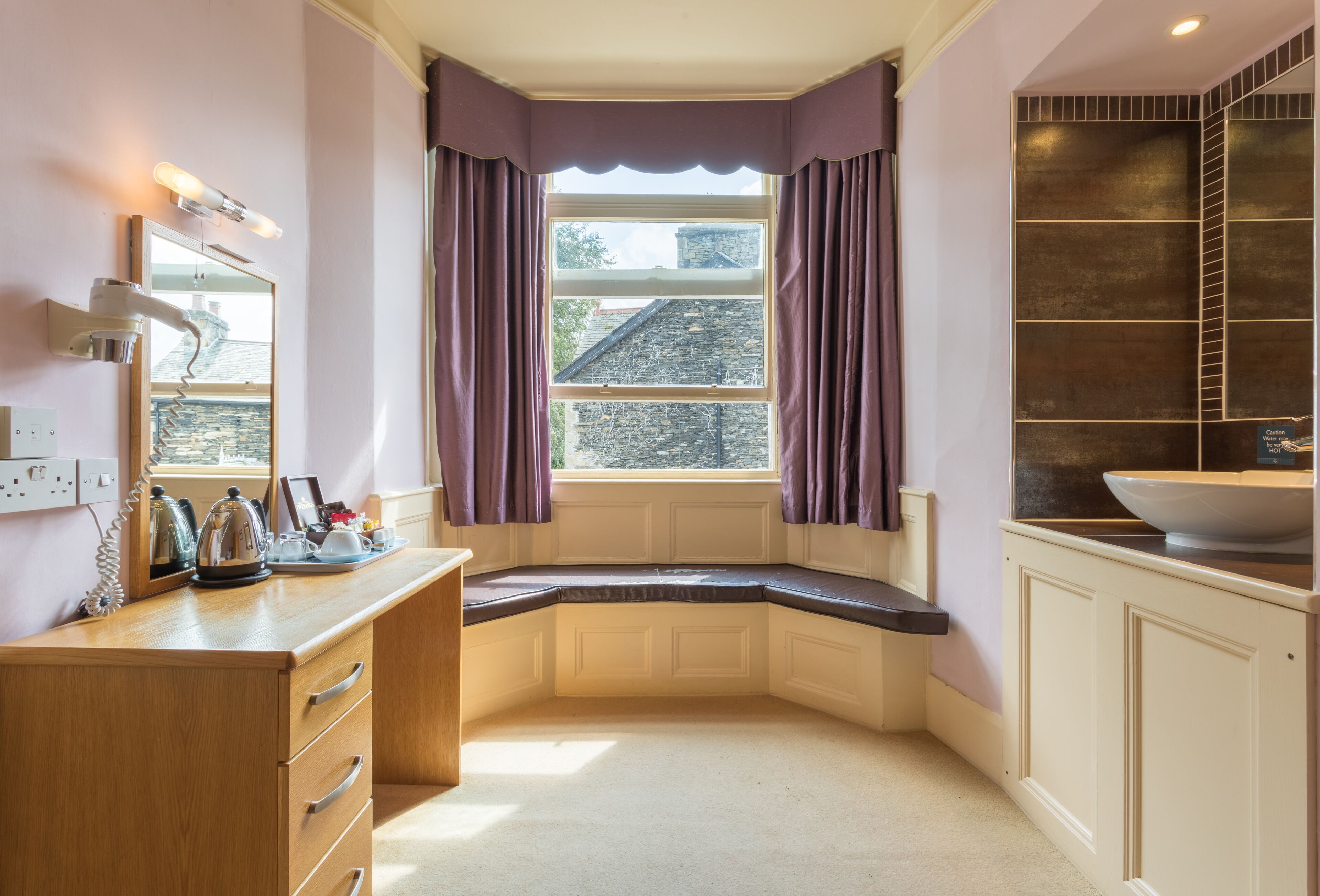 Une petite salle de bain d’angle avec une fenêtre, un miroir, un lavabo et un meuble de rangement.