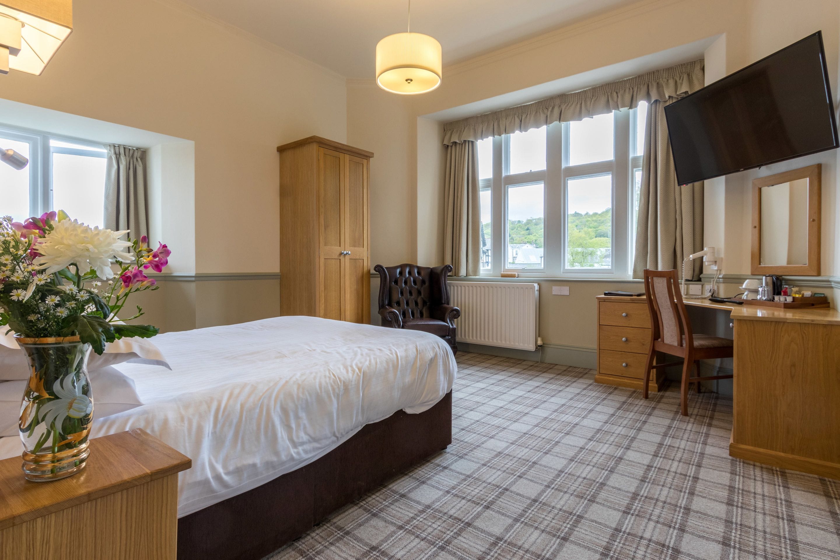 A hotel room with a large bed, a desk, a chair, a TV, and a window with a view.