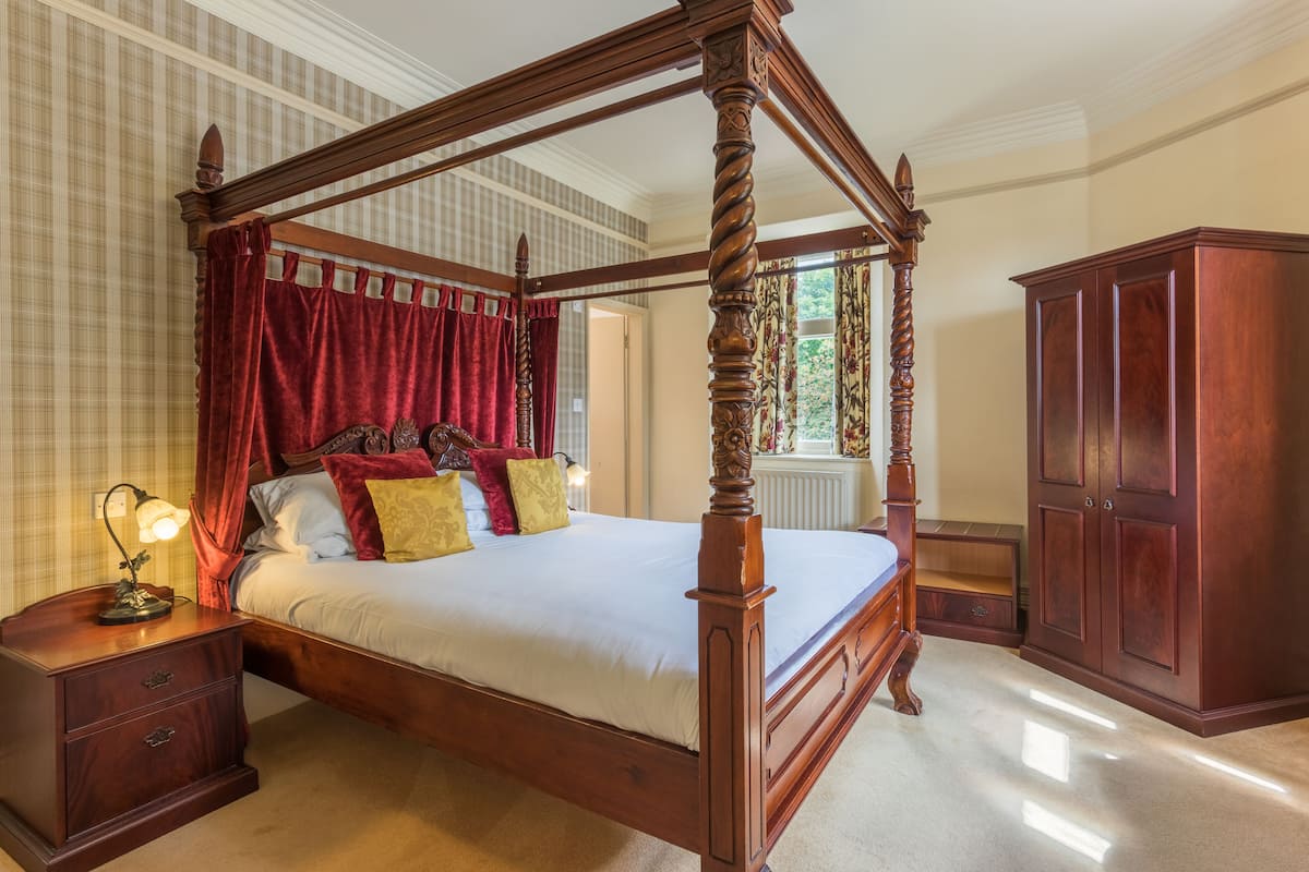 A four-poster bed with red curtains, a nightstand with a lamp, and a wooden wardrobe.