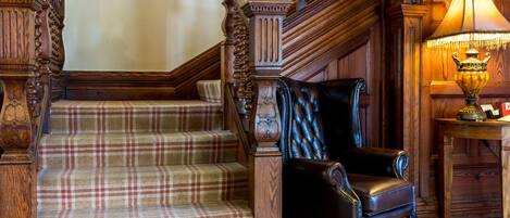 A staircase with a plaid carpet, a leather armchair, and a table with a lamp.