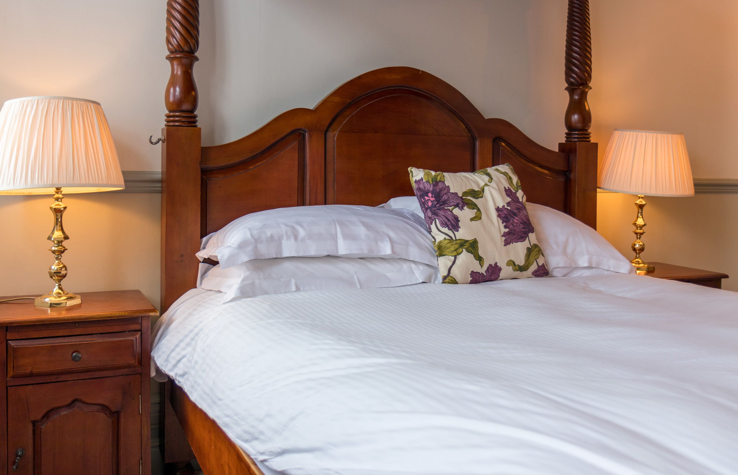 A neatly made bed with white linens and a floral pillow, flanked by two bedside tables with lamps.