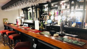 A bar area with a wooden counter, multiple stools, and a variety of bottles and glasses. - The Noel at Whitwell (Oakham)
