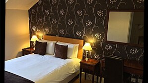 A hotel room with a large bed, two bedside tables, a desk, and a chair. - The Noel at Whitwell (Oakham)