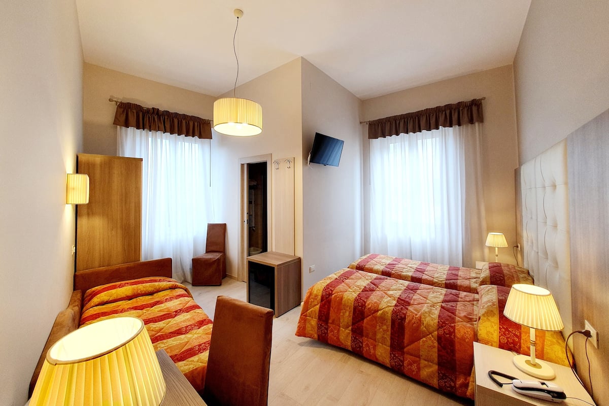A hotel room with two beds, a desk, a chair, a TV, and lamps.