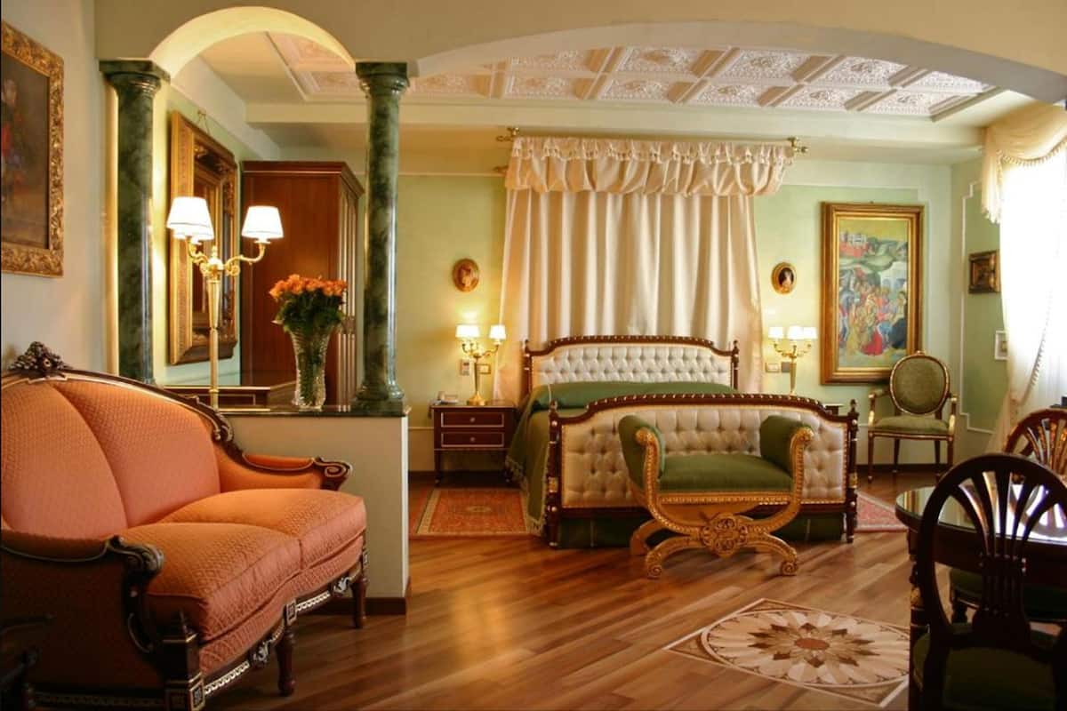 A spacious bedroom with a large bed, a sitting area with a sofa, and a dining table.