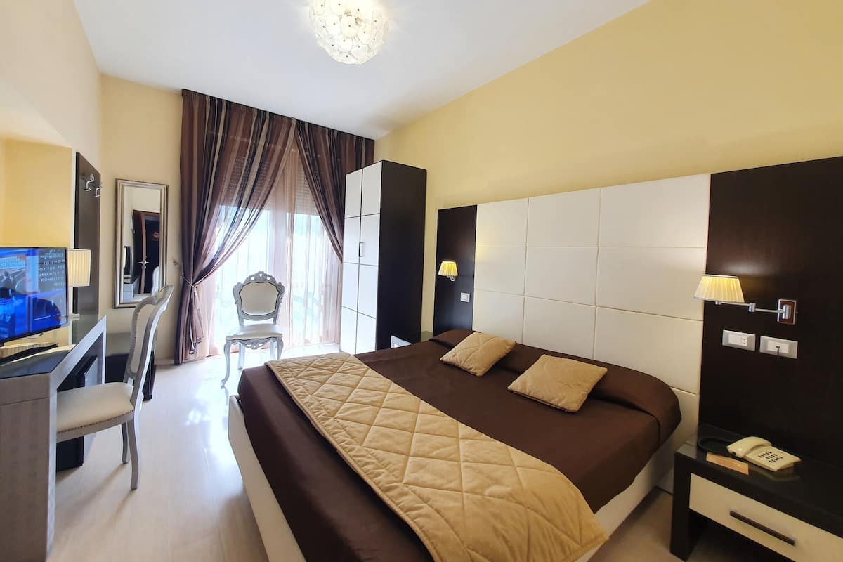 A hotel room with a large bed, a desk with a TV, a chair, and a wardrobe.