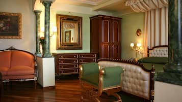 A room with a green upholstered armchair, a wooden cabinet, a large mirror, and a bed with green bedding.