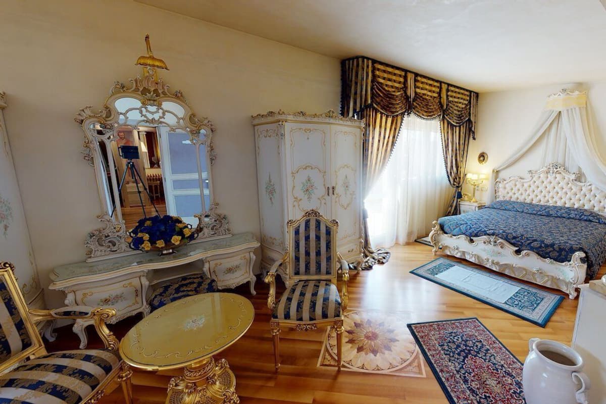 A luxurious bedroom with ornate furniture, a large bed with a canopy, a chandelier, and a mirror.