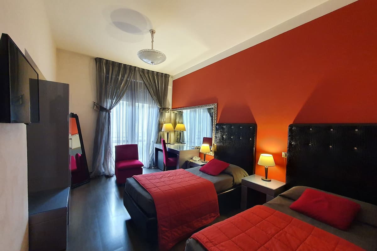 A hotel room with two beds, a desk, a chair, a TV, and a ceiling fan.