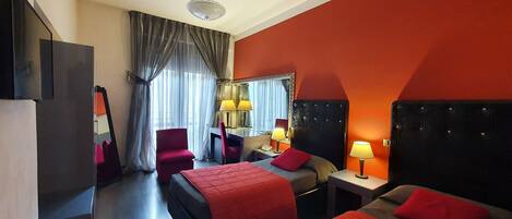 A hotel room with two beds, a desk, a chair, a TV, and a ceiling fan.