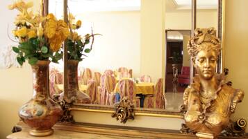 An ornate mirror with a gold frame, a bust sculpture, and a vase with flowers on a marble console table.