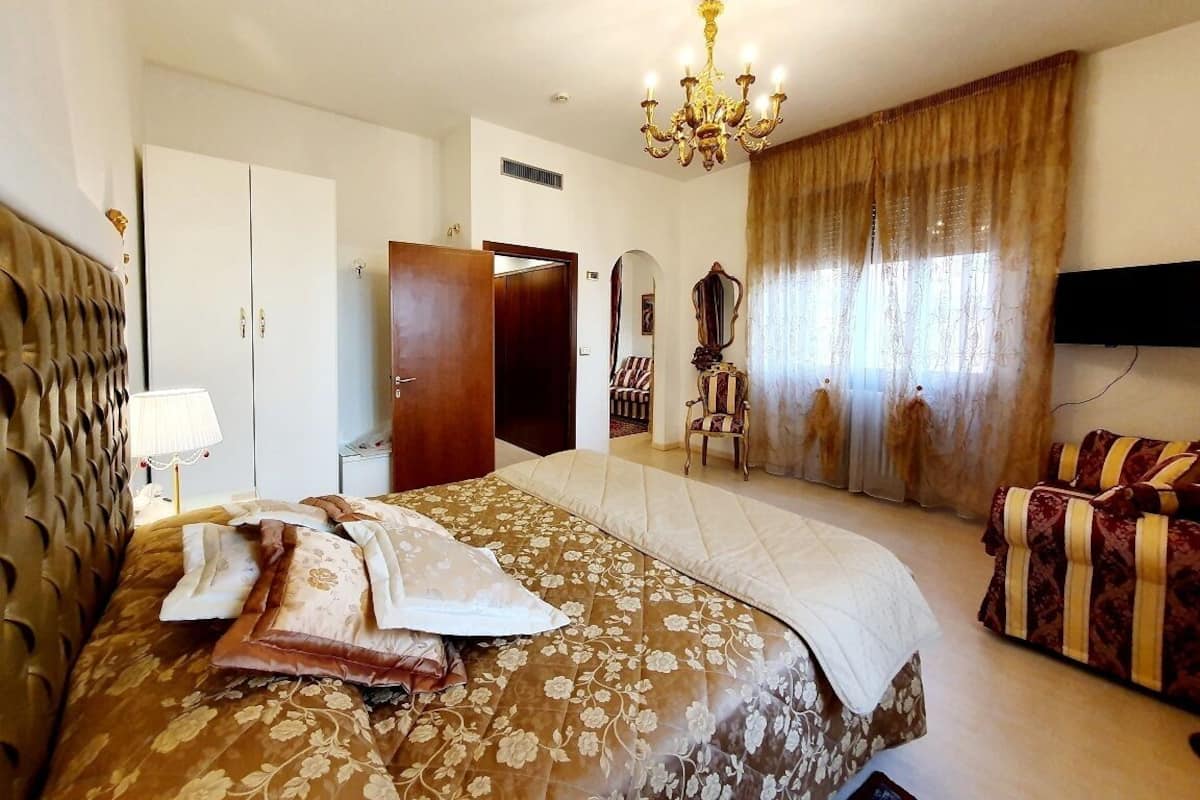 A hotel room with a large bed, a chandelier, a television, and a wardrobe.