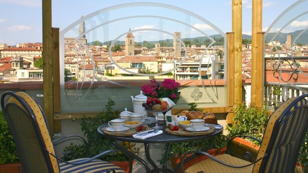 Un balcon avec une table dressée pour le petit-déjeuner, offrant une vue sur un paysage urbain avec des bâtiments historiques et une rivière.