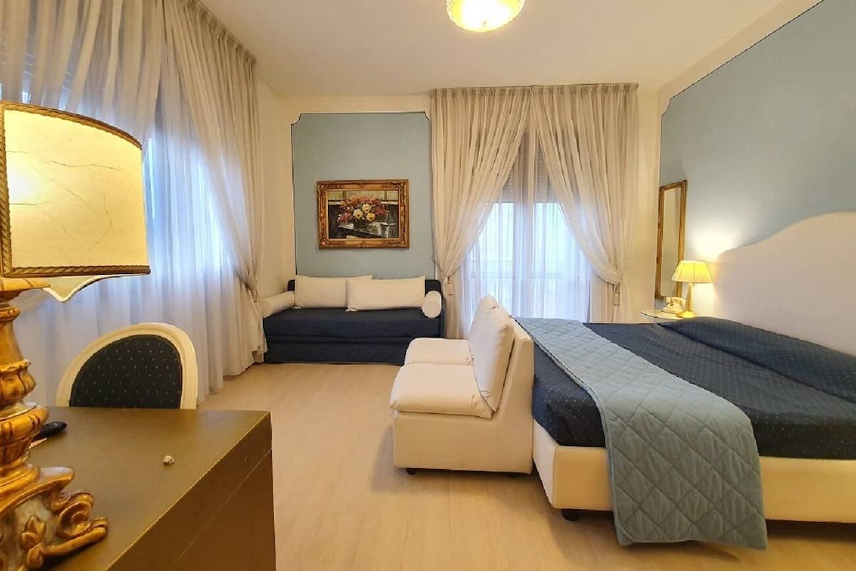 A hotel room with a bed, a sofa, a desk, and a lamp.