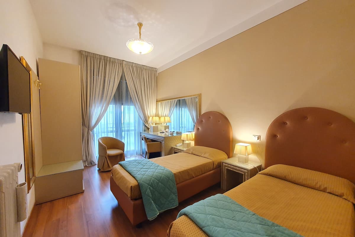 A hotel room with two beds, a desk, a chair, a mirror, and a ceiling light.