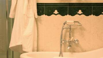 Un baño con una bañera independiente, una toalla colgada en la pared y un estante pequeño con artículos de aseo.