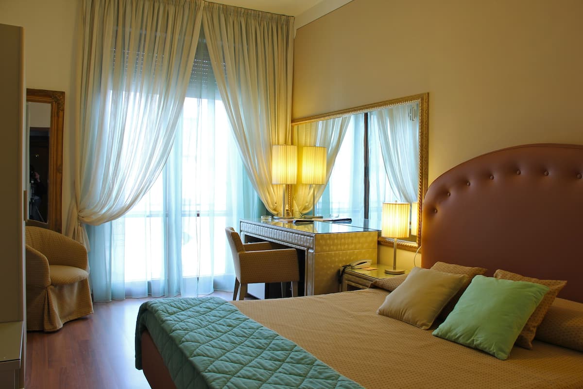 A hotel room with a bed, a desk, a chair, and a large mirror.