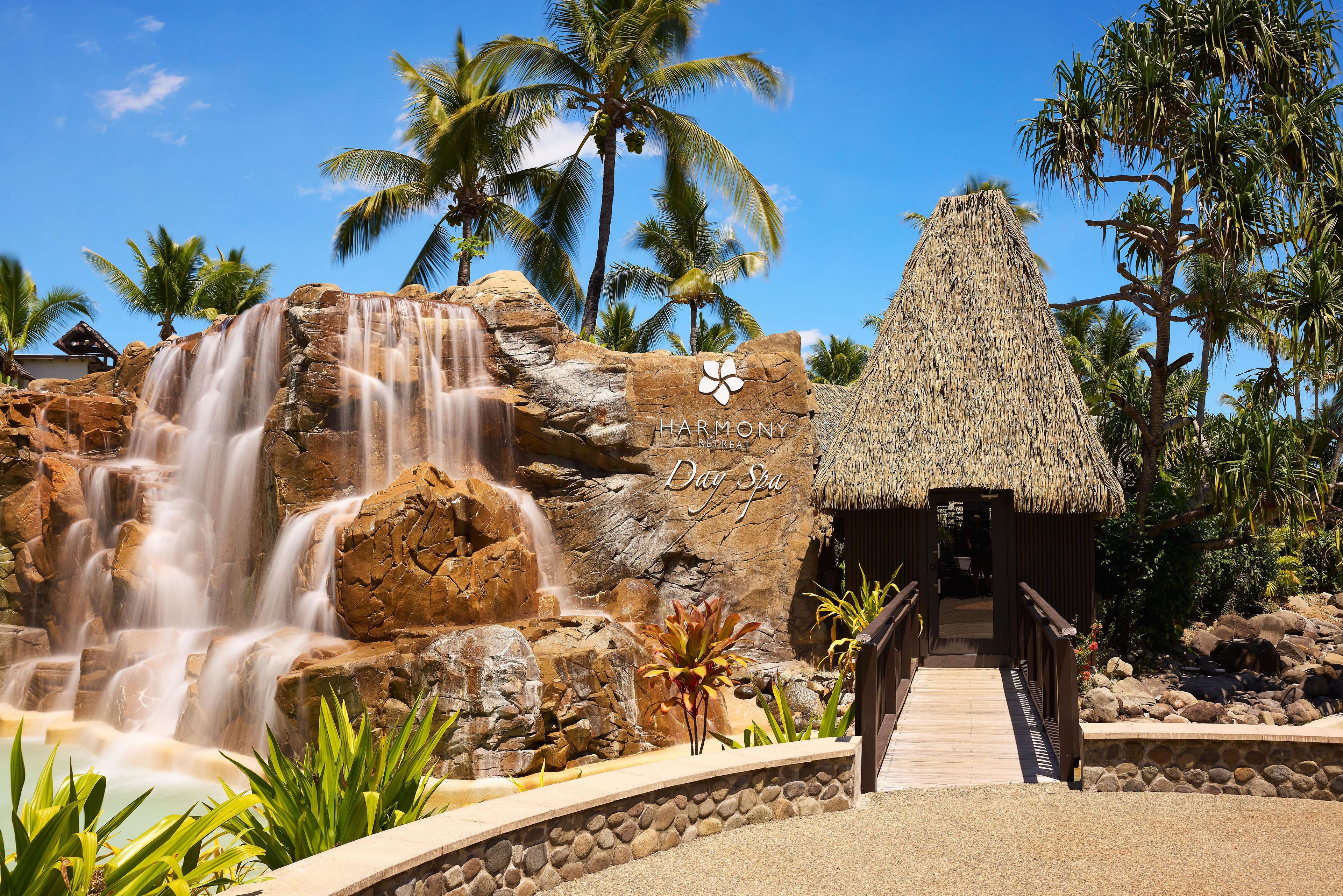 A waterfall, palm trees, and a thatched-roof structure.