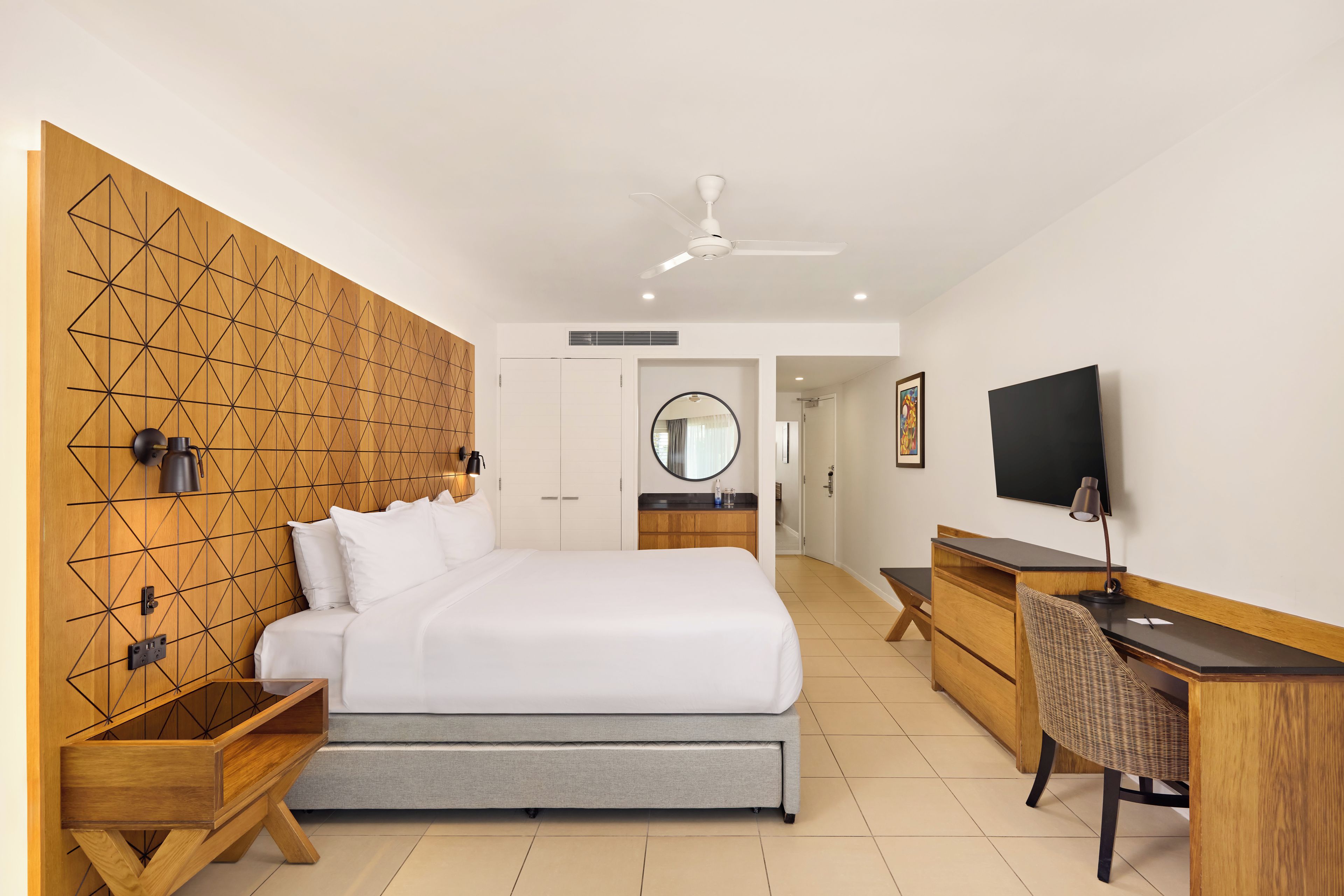 A modern hotel room with a large bed, a desk, a chair, a television, and a ceiling fan.