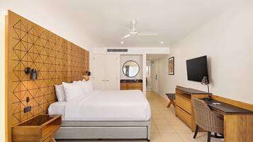 A modern hotel room with a large bed, a desk, a chair, a television, and a ceiling fan.
