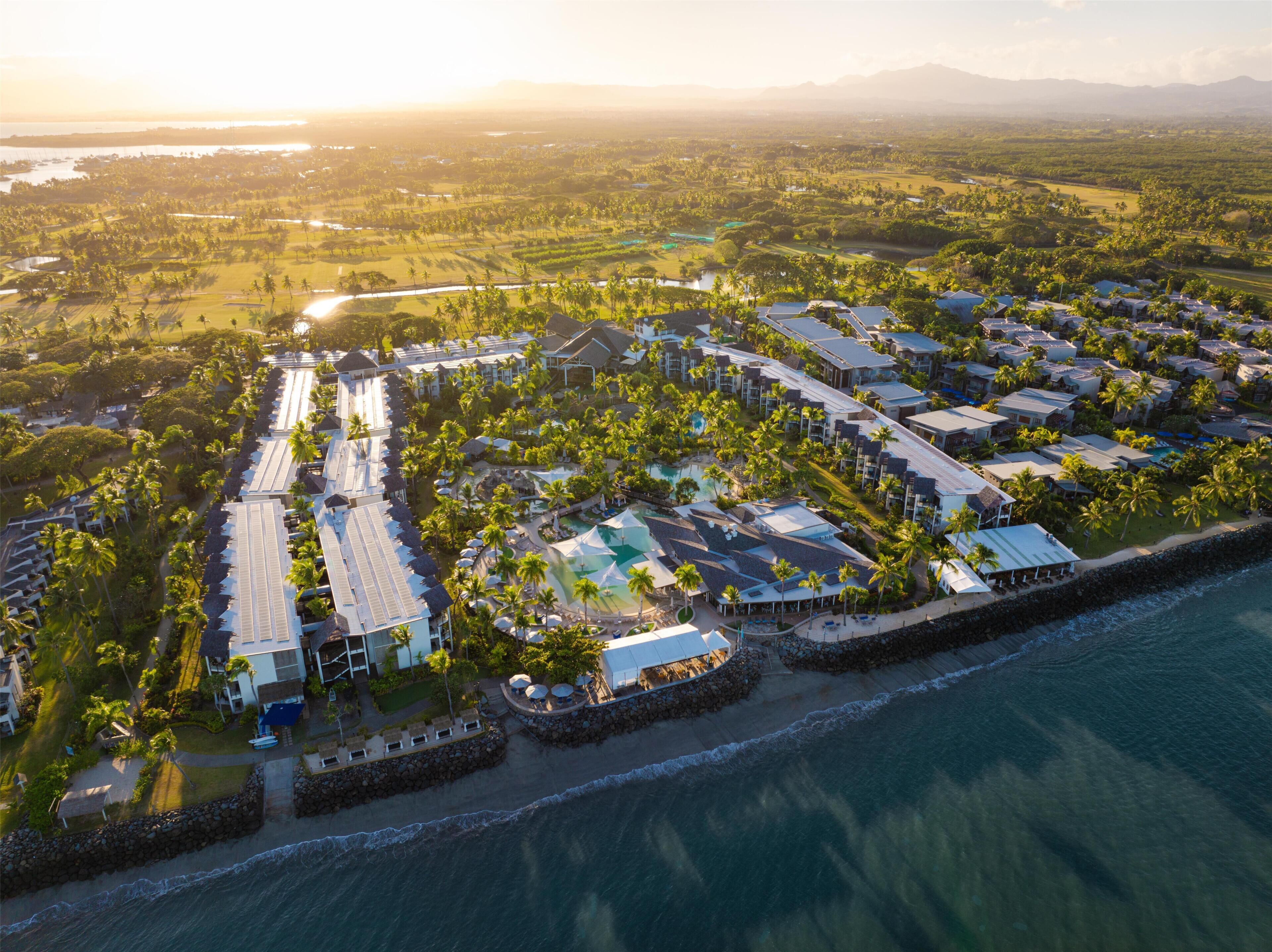 An aerial view of a resort with multiple buildings, a beachfront, and a large pool area.