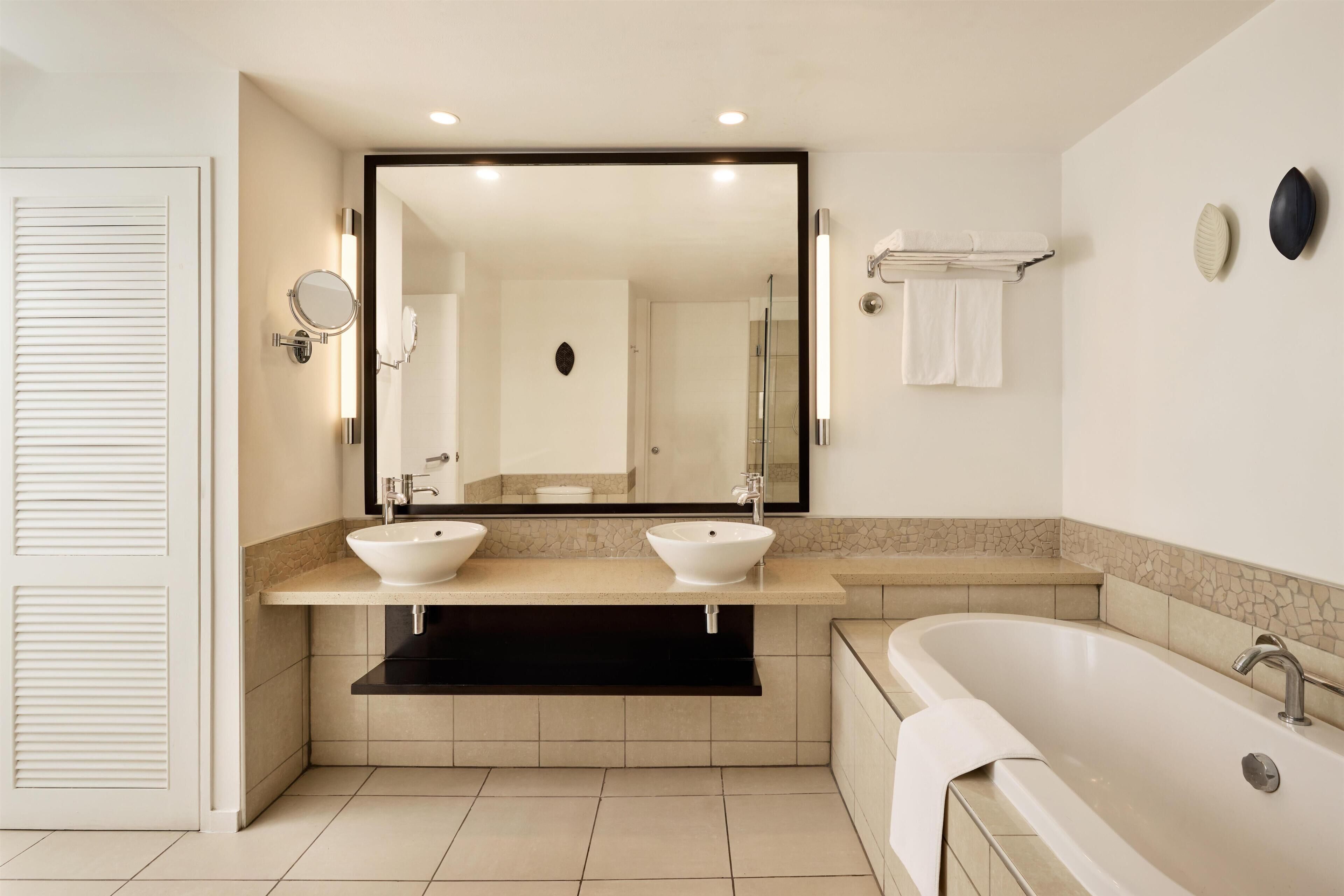 A modern bathroom with two sinks, a large bathtub, and a mirror with lights.