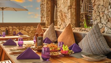 A wooden table set with purple napkins, plates, and glasses, with stone walls and a view of the sky.