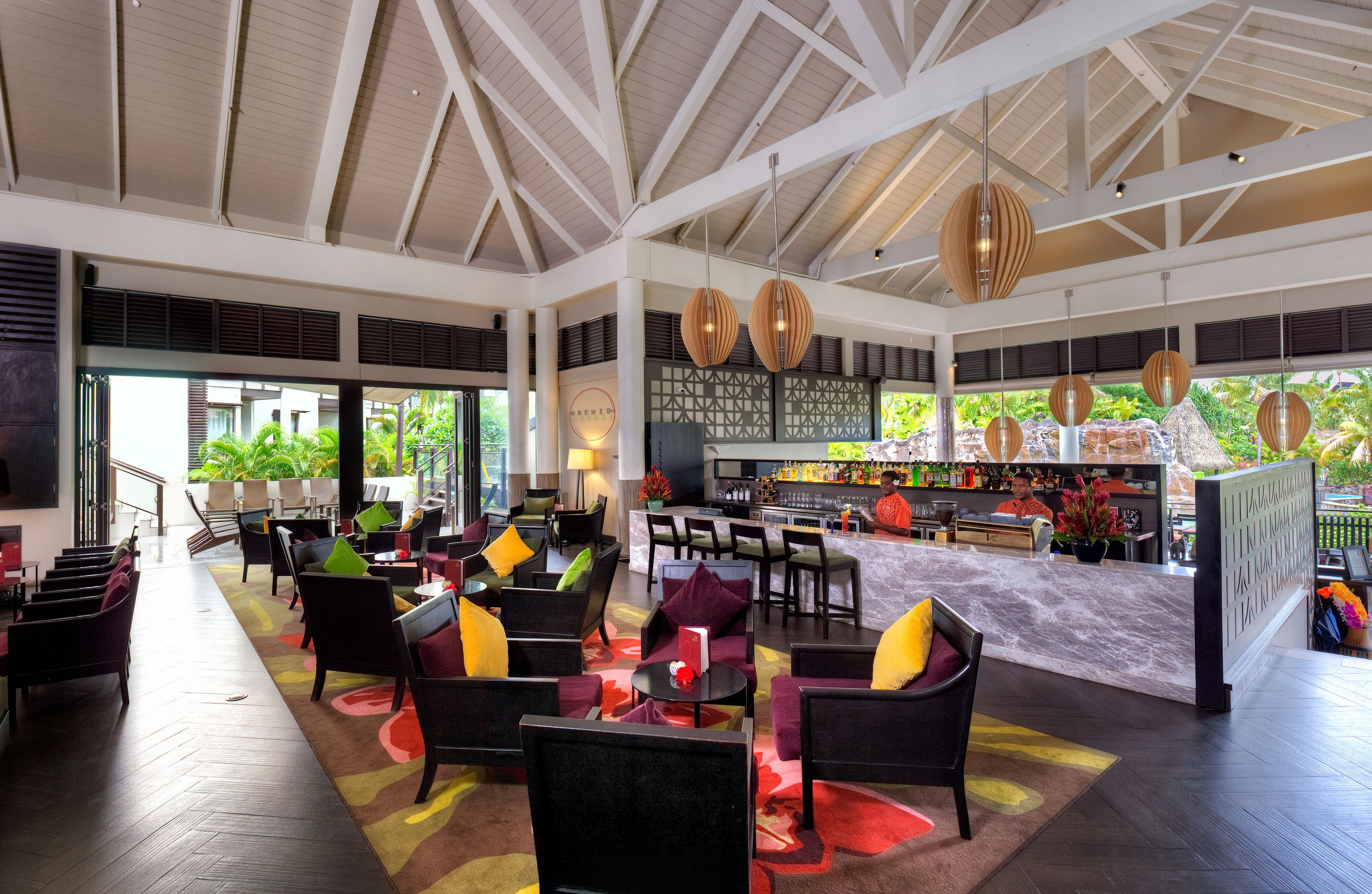 A spacious lobby with a high ceiling, multiple seating areas, a bar, and large windows offering a view of greenery outside.