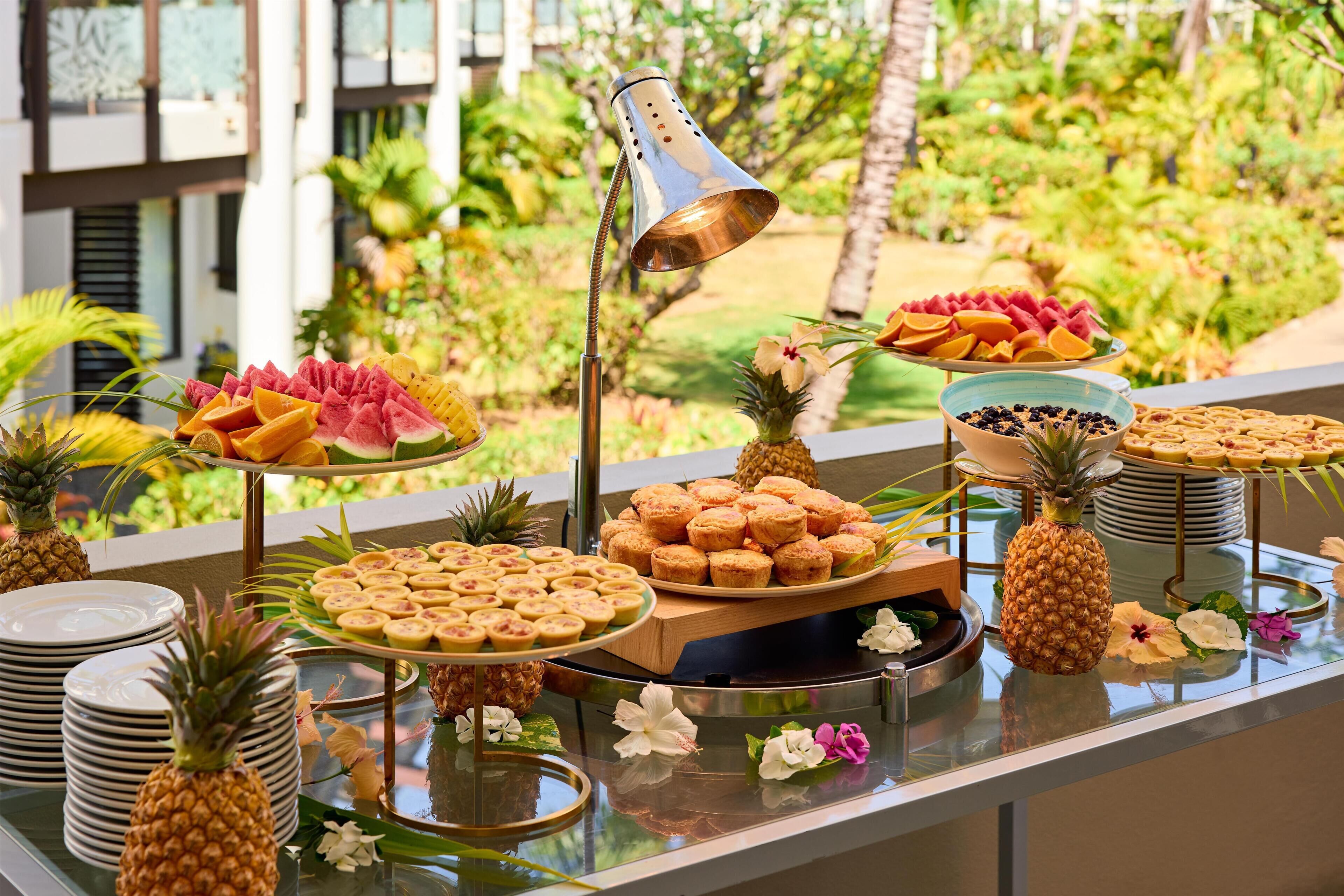 Un bufé con frutas tropicales, pastelería y una lámpara decorativa.