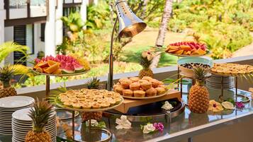 Un bufé con frutas tropicales, pastelería y una lámpara decorativa.