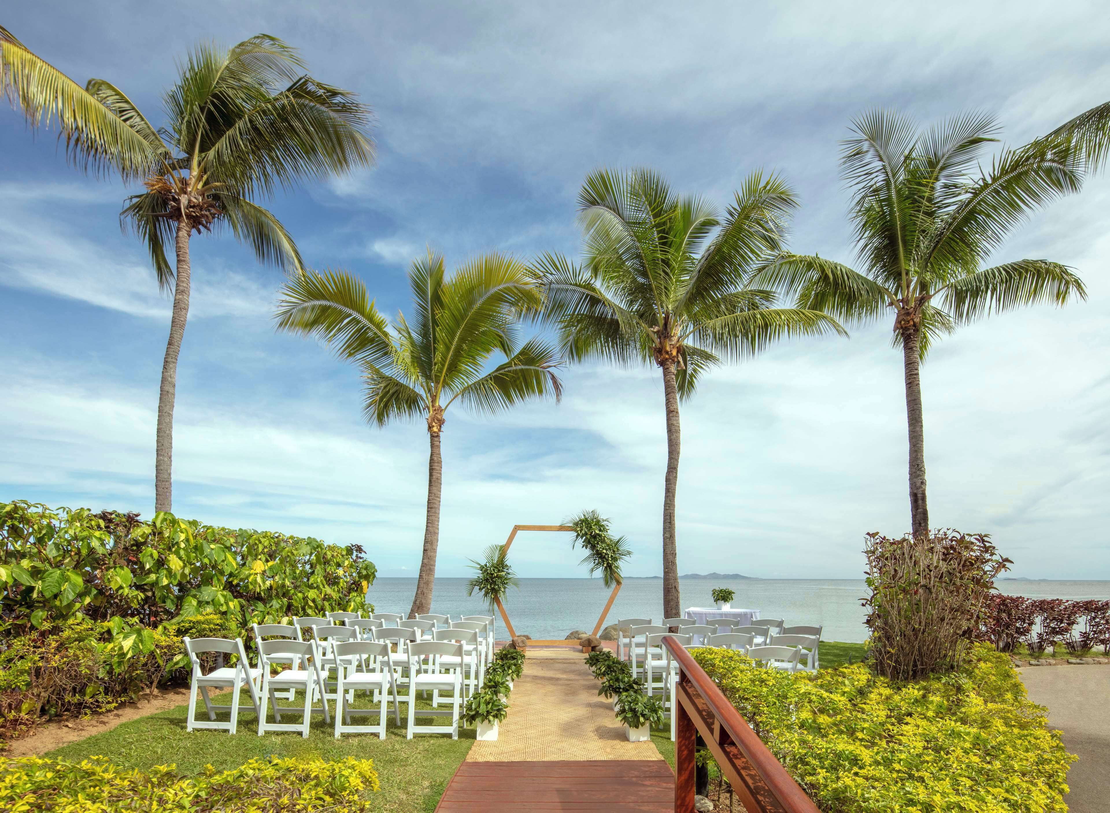 A beachside wedding setup with white chairs and a wooden walkway leading to the sea.