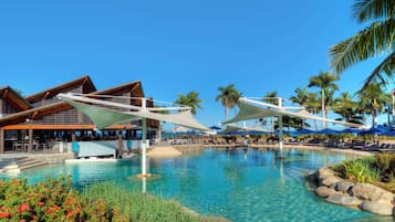 Un espace piscine aménagé dans un complexe hôtelier, avec des chaises longues, des parasols et un bâtiment à la façade en bois.
