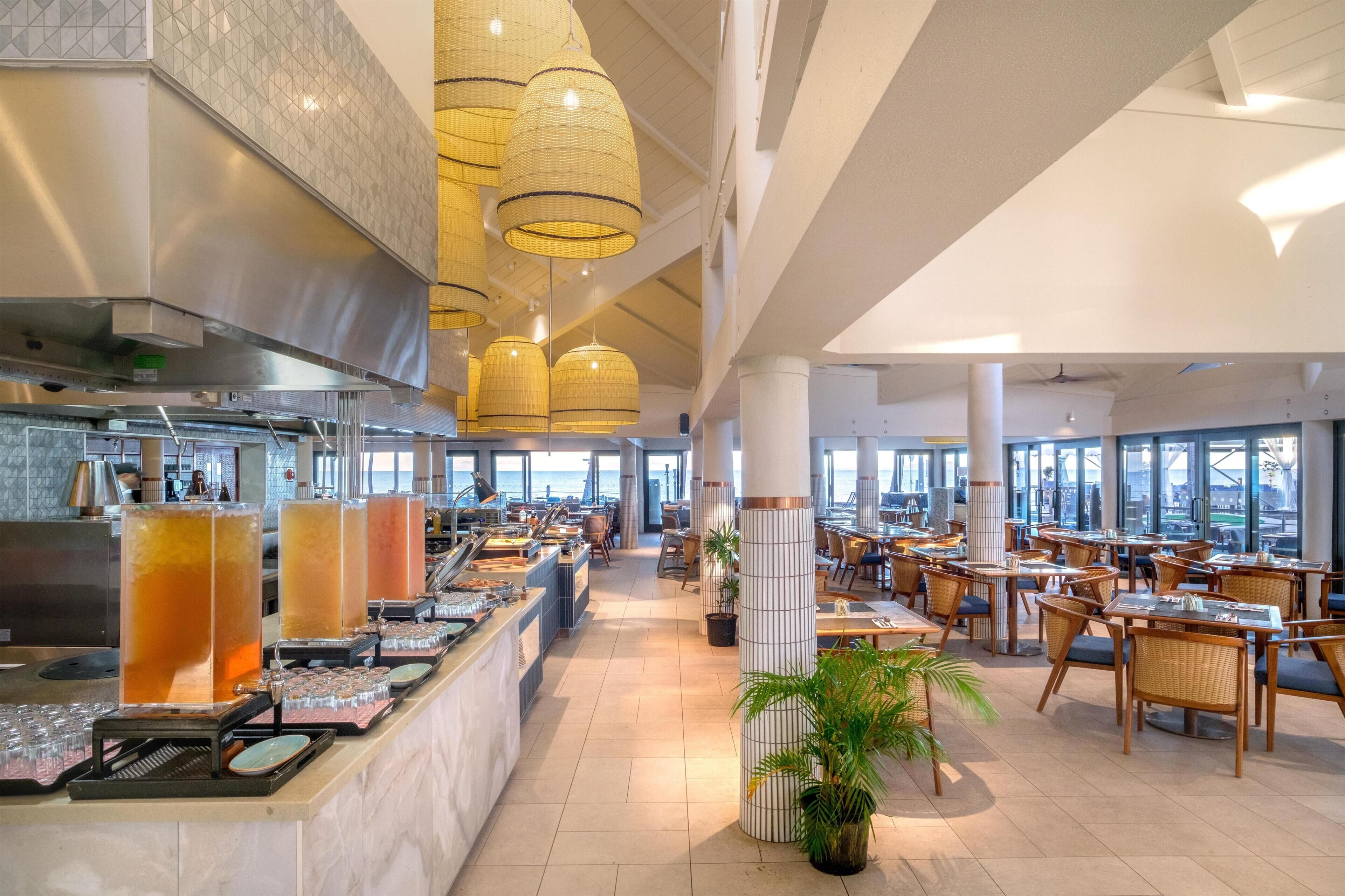 Un restaurant spacieux avec de hauts plafonds, de grandes fenêtres et un espace buffet.