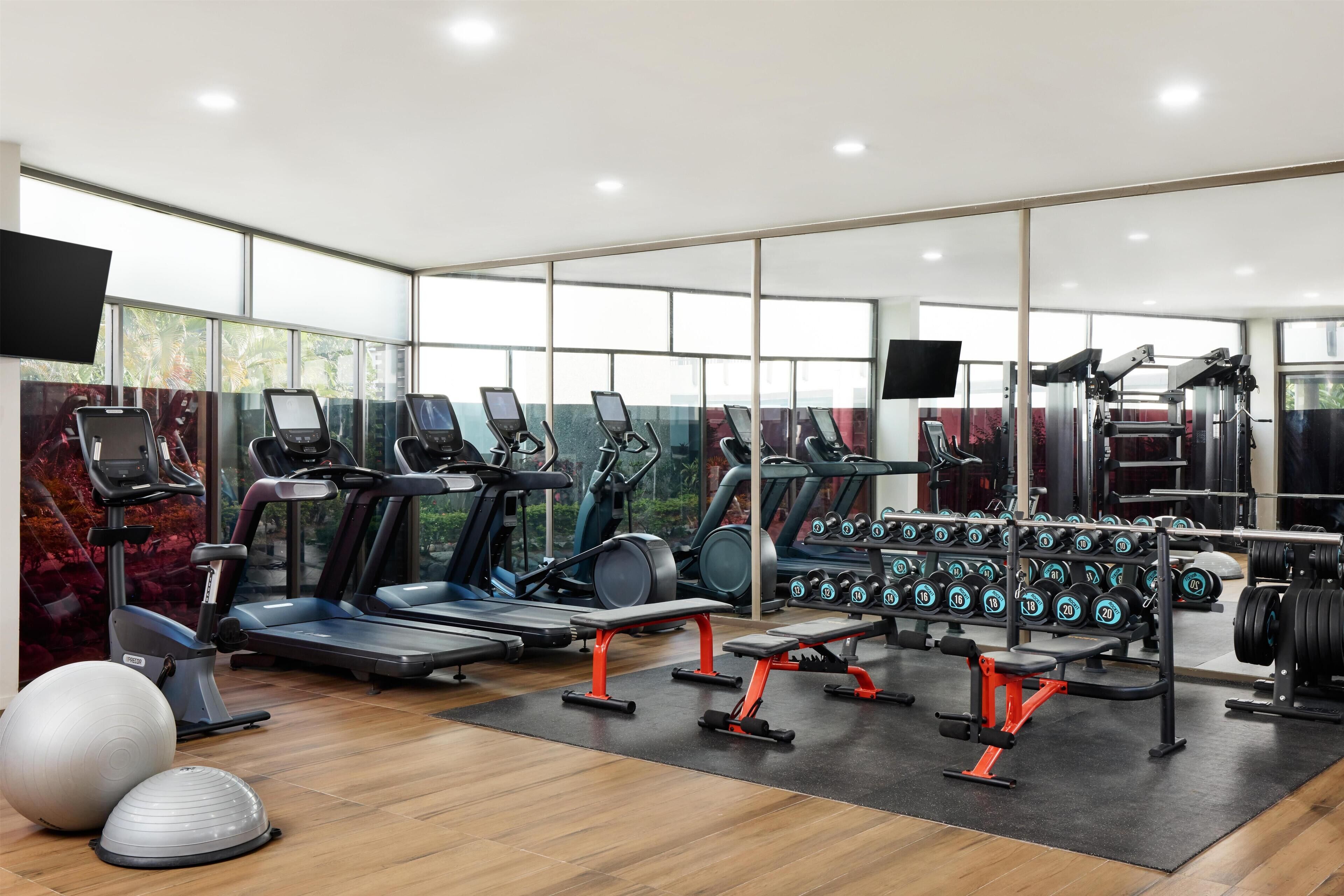 A modern gym with treadmills, elliptical machines, weight benches, and dumbbells.