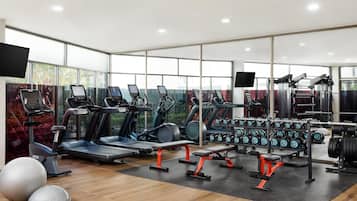 A modern gym with treadmills, elliptical machines, weight benches, and dumbbells.