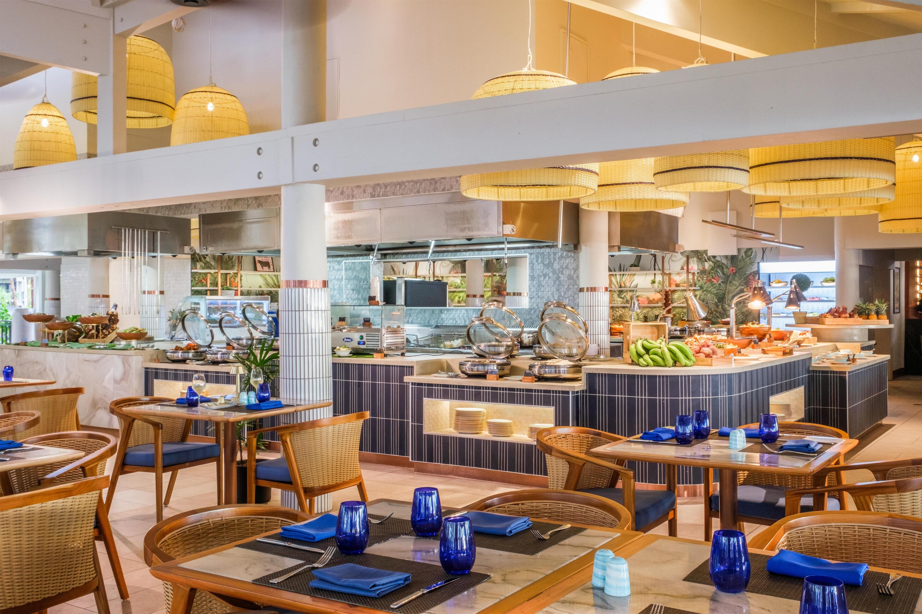 A restaurant with wicker furniture, blue napkins, and a buffet area with various food items.